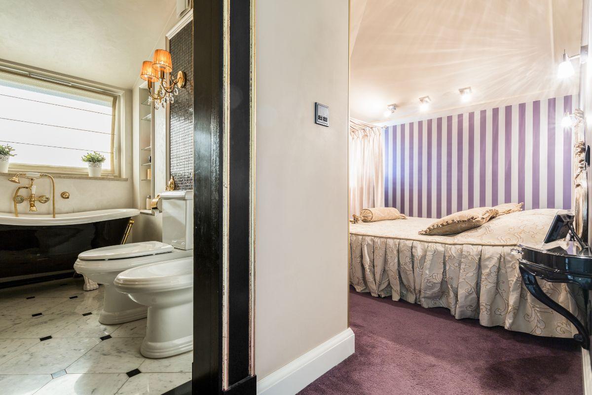 Luxurious bathroom with marble floors, a clawfoot tub, and an adjoining bedroom with purple striped walls and elegant bedding.