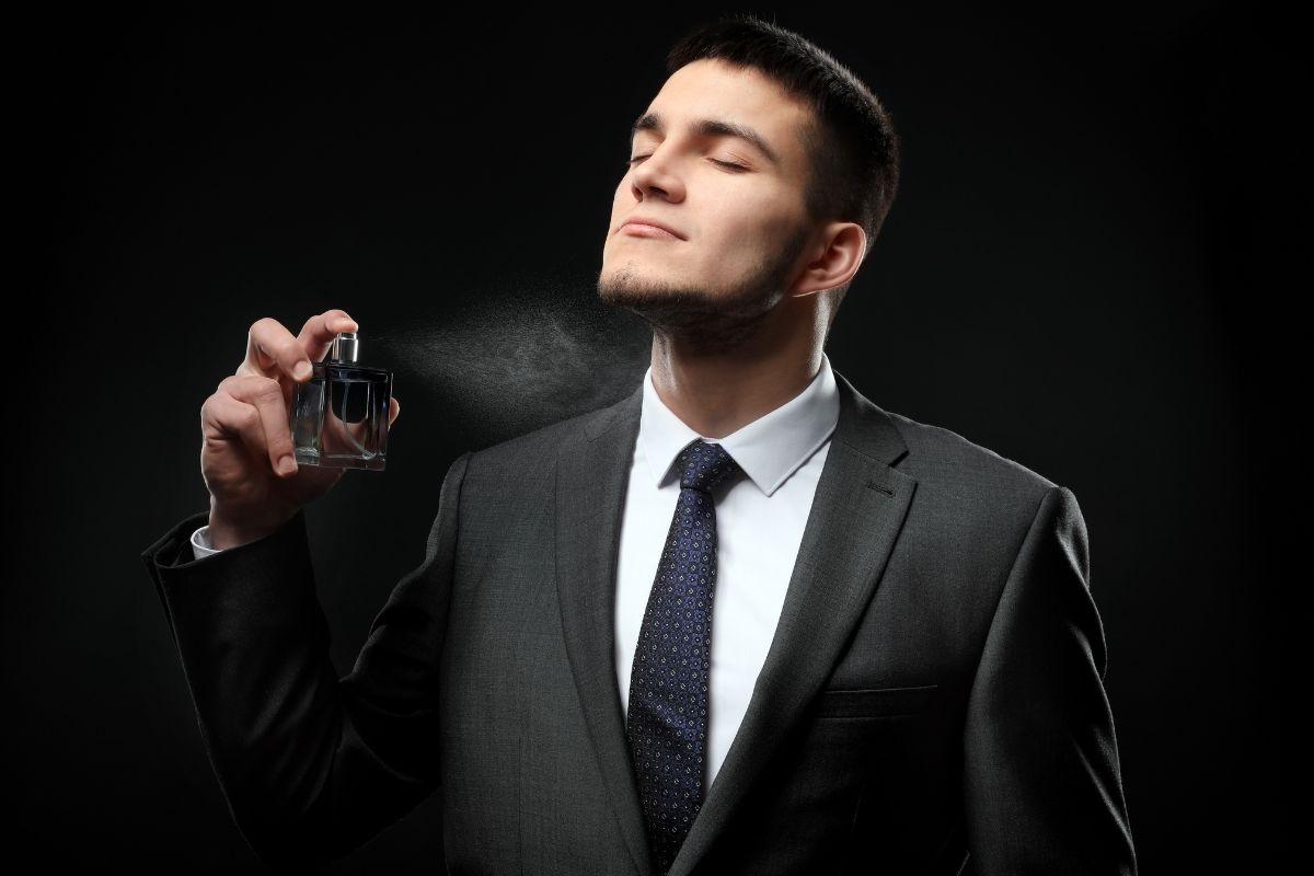 Man in a suit spraying cologne on himself against a dark background.