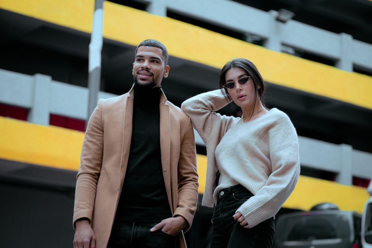 Fashionable man and woman posing outdoors in front of a building with a yellow and gray background.