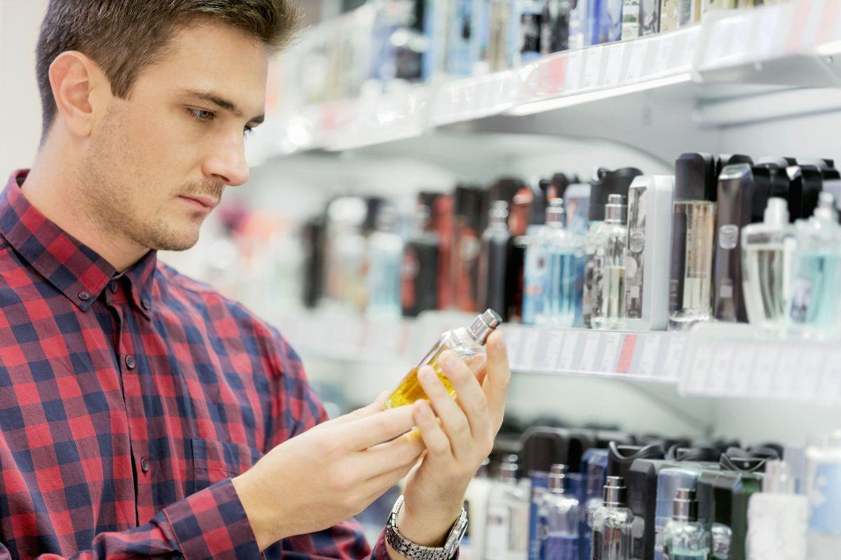 Man in a plaid shirt examining a bottle of perfume in a store aisle filled with various fragrances.