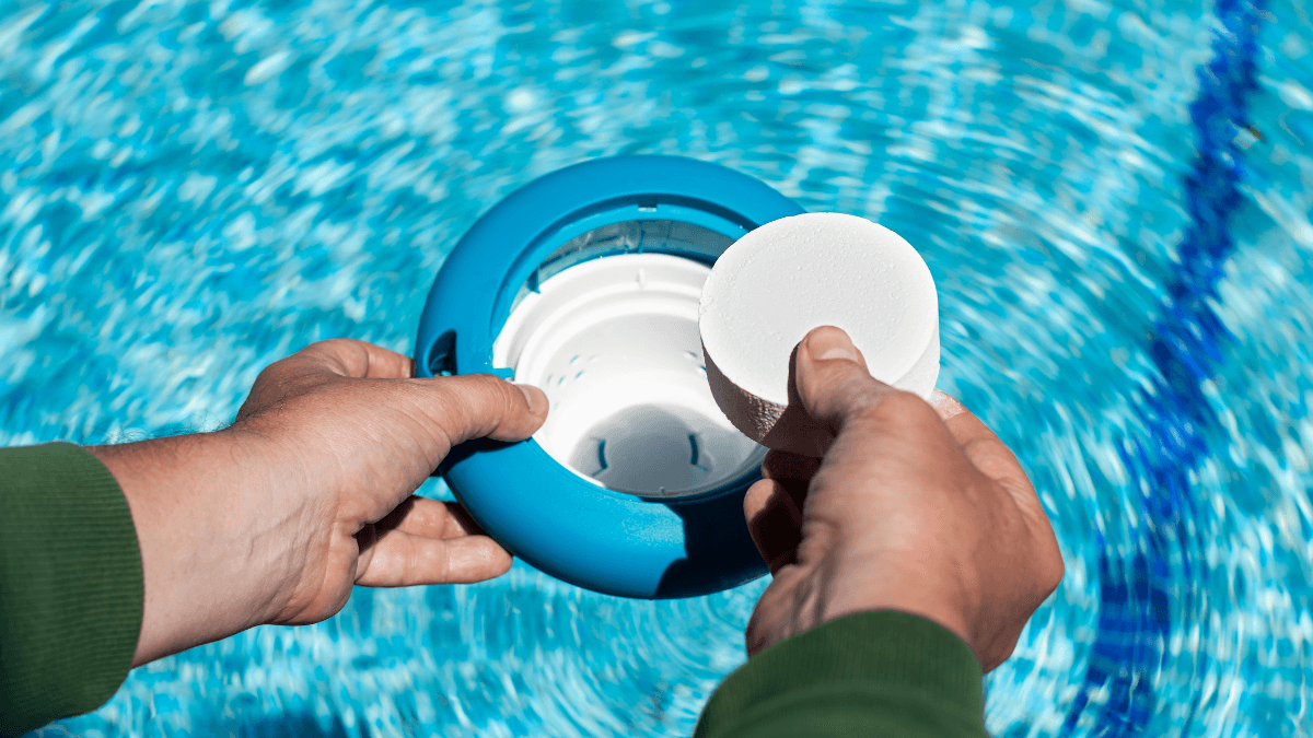 Hand placing a chlorine tablet into a floating dispenser for pool maintenance, ensuring clear and hygienic swimming water.