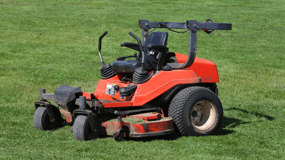 Red riding lawn mower parked on a lush green lawn, showcasing its sturdy build and dual cutting blades for efficient grass trimming.