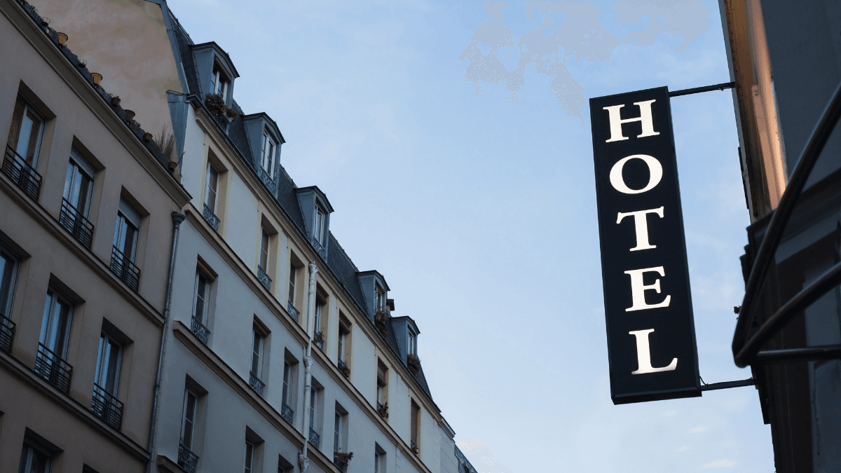 Street view of a traditional hotel building with a prominent 'Hotel' sign against a clear blue sky, showcasing classic architecture and inviting ambiance.