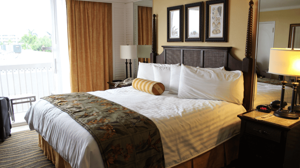 Inviting hotel room featuring a cozy bed with decorative pillows and a patterned runner, elegant table lamps, and framed artwork, complemented by warm lighting and a private balcony view.