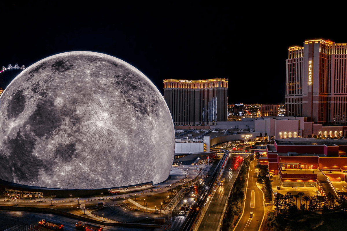 A massive sphere displaying a realistic moon surface illuminates the Las Vegas skyline at night, surrounded by hotels and city lights.