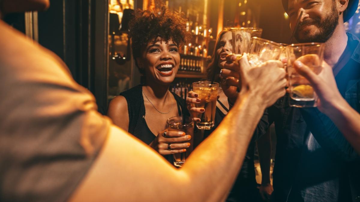 Friends sharing drinks and laughing at a bar, capturing the fun social vibe often paired with Flaviar tasting boxes and whiskey sampling nights.