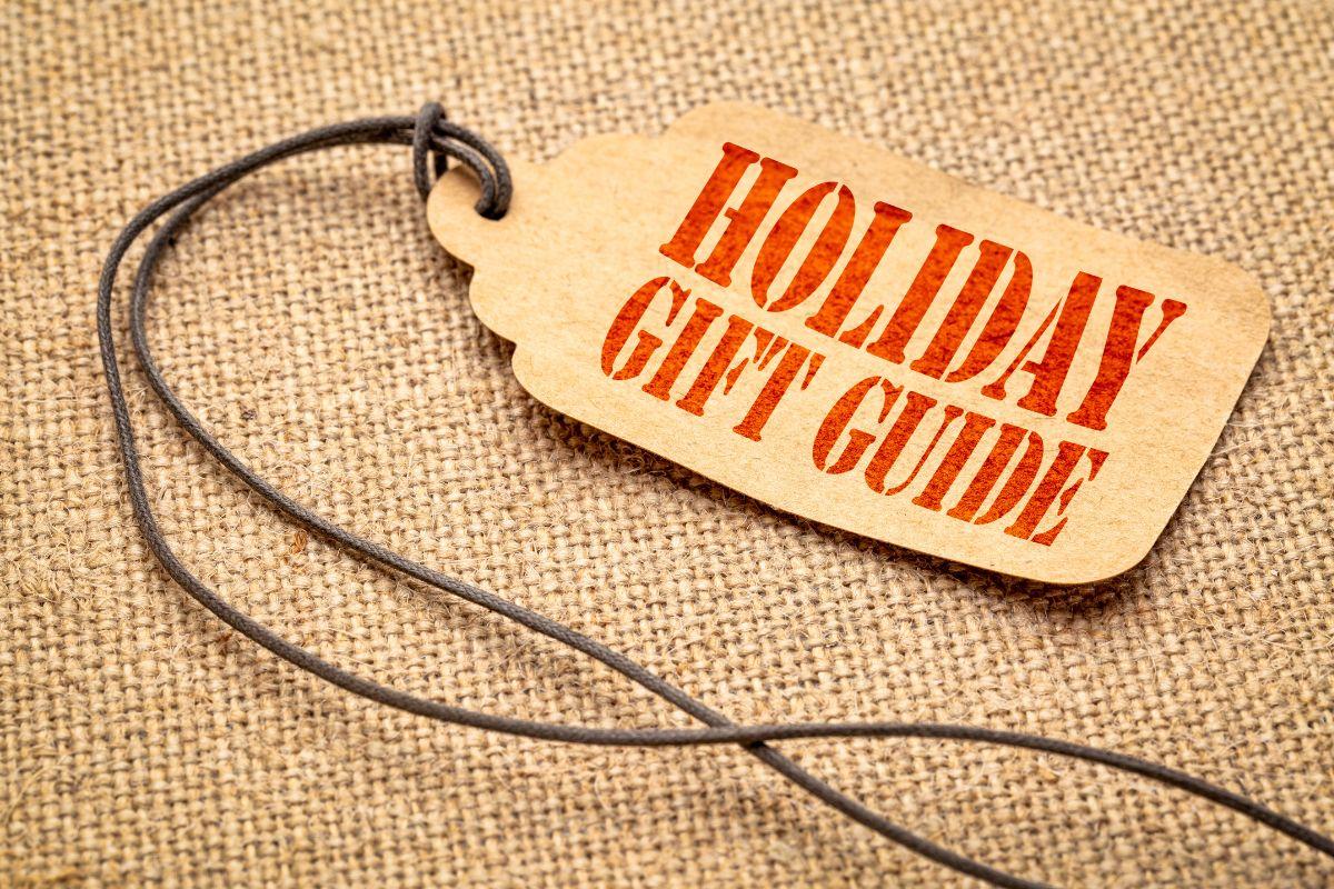 A brown tag with red text reading 'Holiday Gift Guide' on a burlap background, attached to a black string.