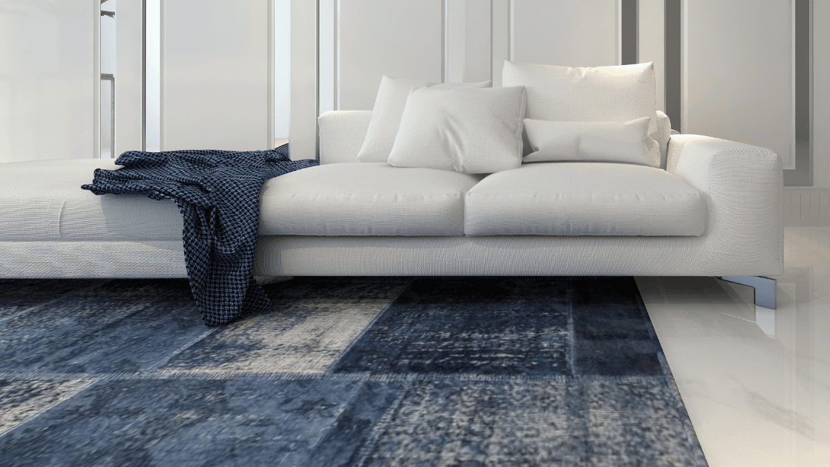 Modern living room with a plush white sofa adorned with cozy pillows, a navy blue throw, and a textured blue area rug, creating a serene and elegant ambiance.