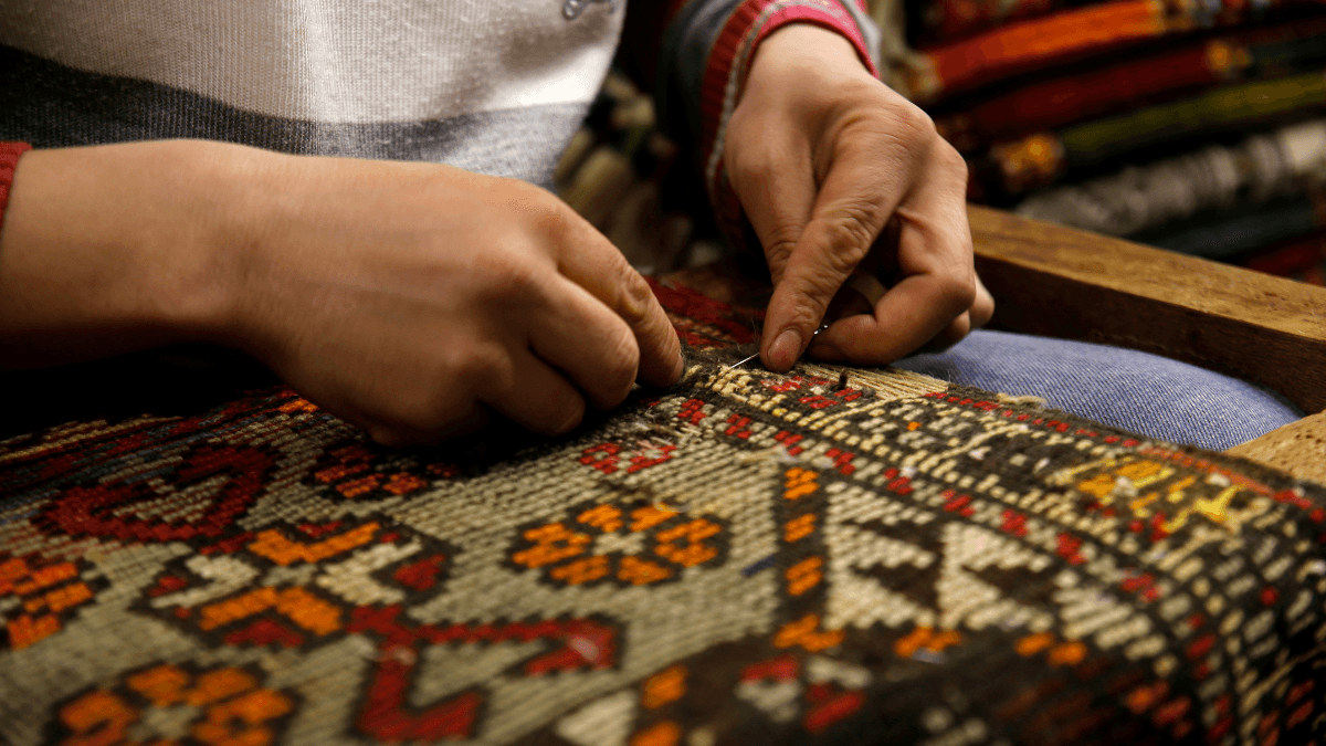 Artisan hands meticulously weaving a colorful, traditional carpet, highlighting the intricate patterns and craftsmanship of handmade textiles.