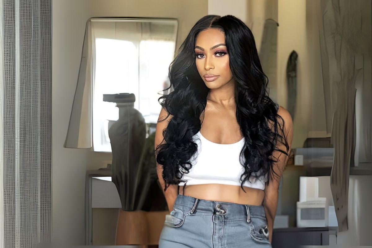 Woman with long, wavy black hair wearing a white crop top and jeans, standing in a room with a mirror and modern decor.