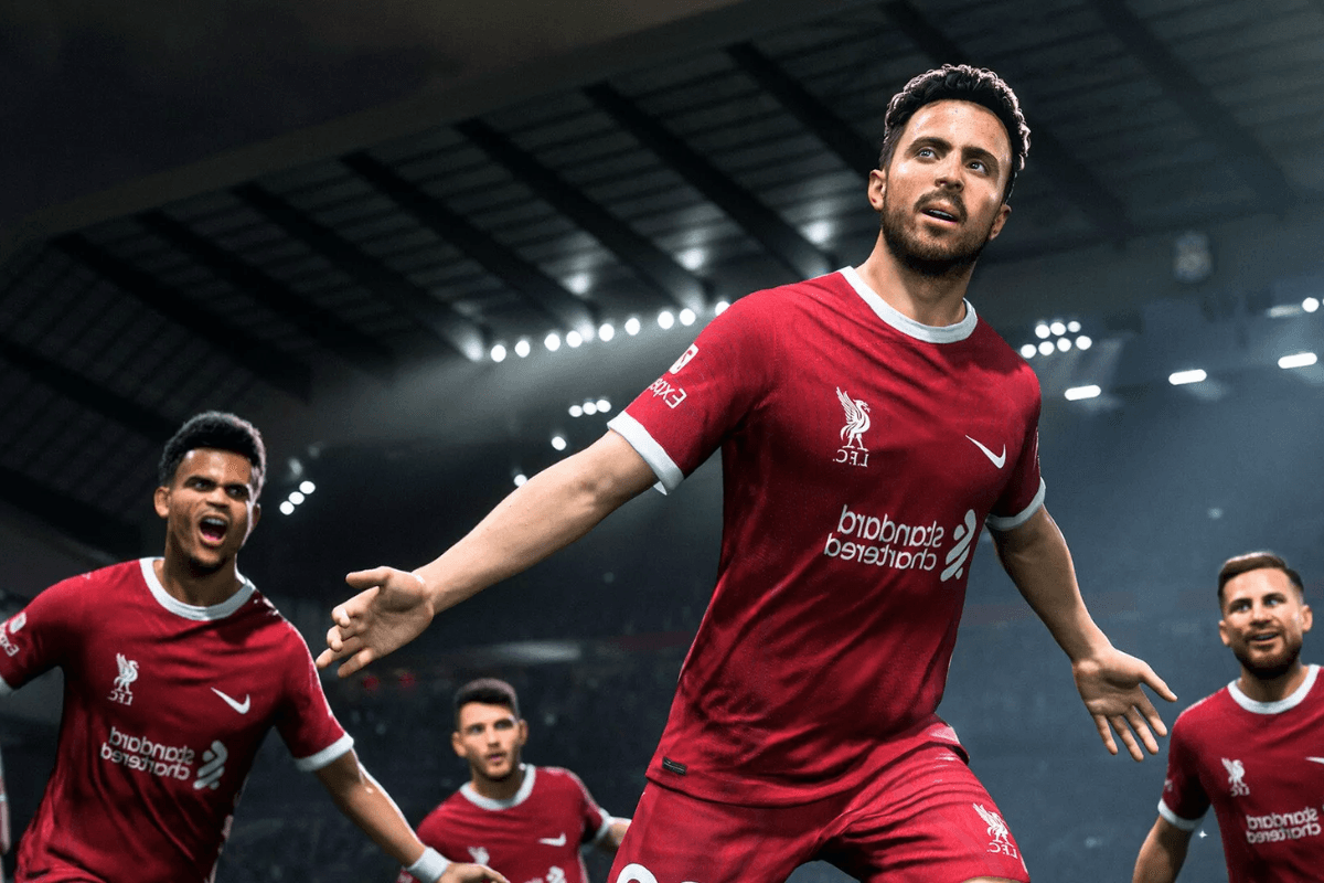 A soccer player in a red Liverpool FC jersey celebrates a goal with teammates in a brightly lit stadium.