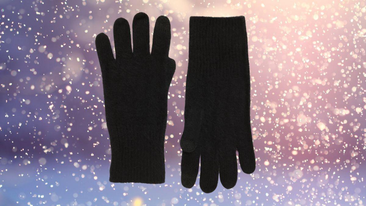 A pair of black brushed cashmere tech gloves displayed against a soft winter background with falling snowflakes.