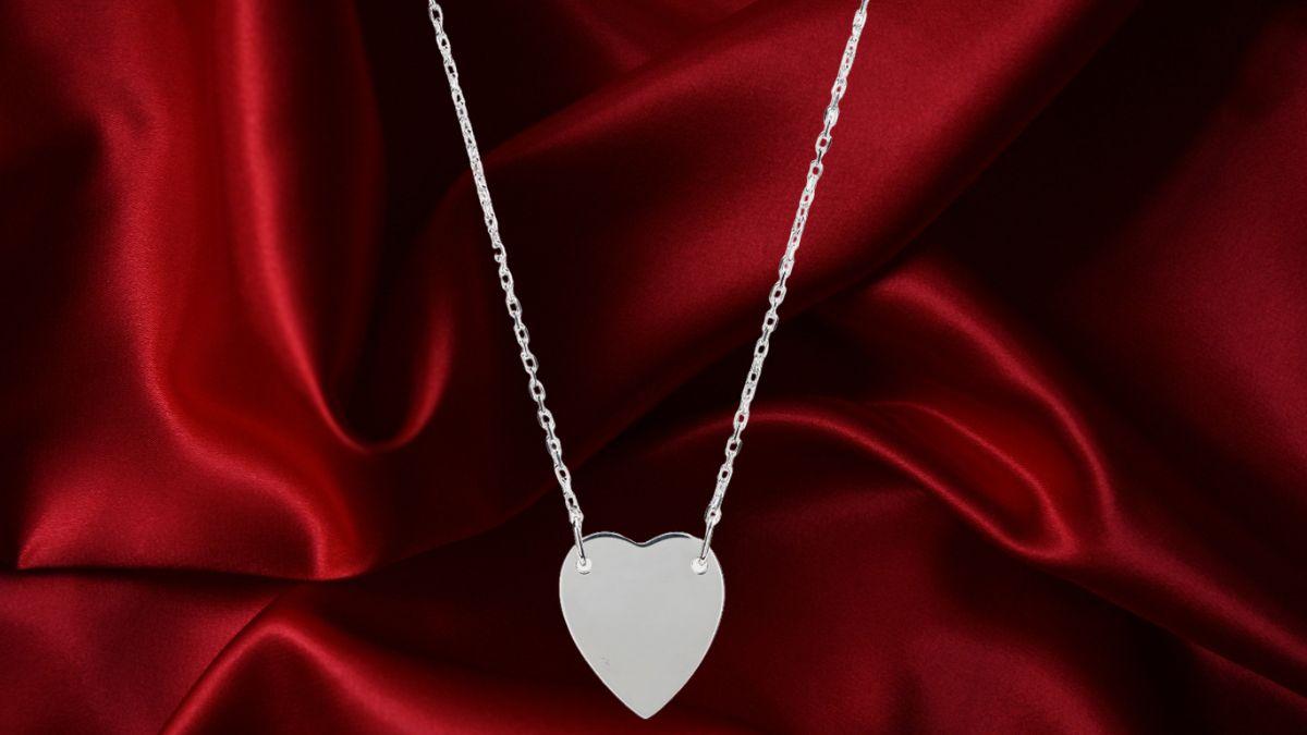 A close-up of a silver heart-shaped necklace displayed on a rich red satin fabric background.