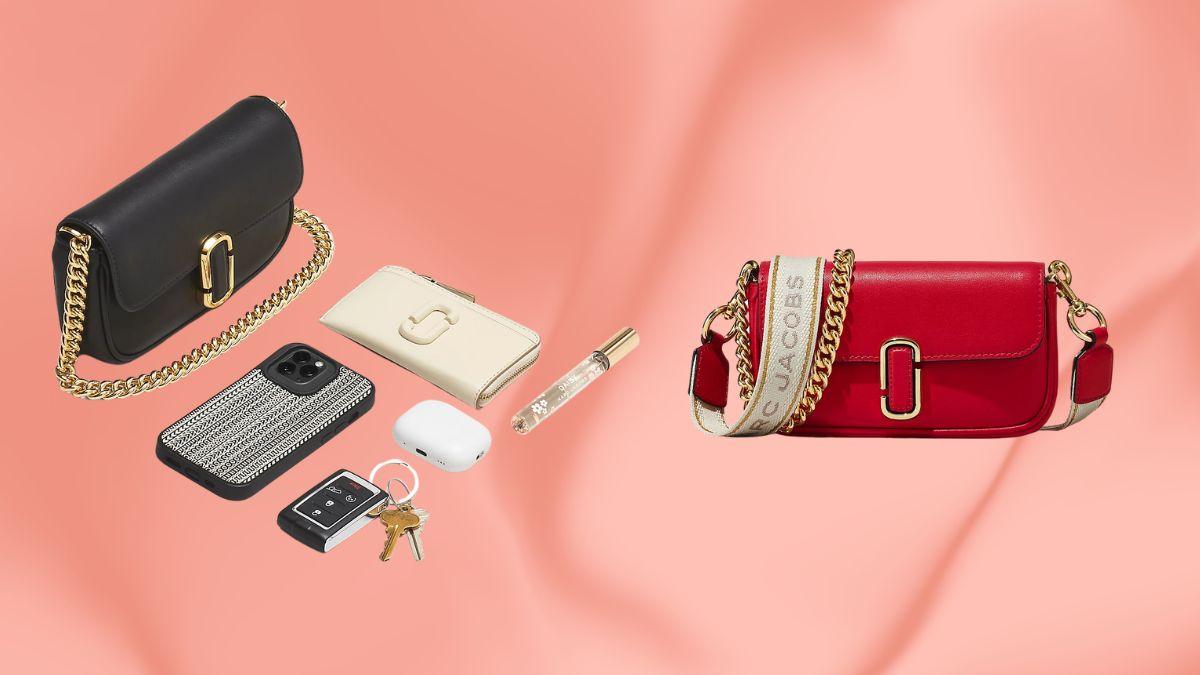 A black and a red Marc Jacobs J Marc Mini Bag are shown with everyday essentials like a wallet, phone, keys, and perfume on a soft pink background.