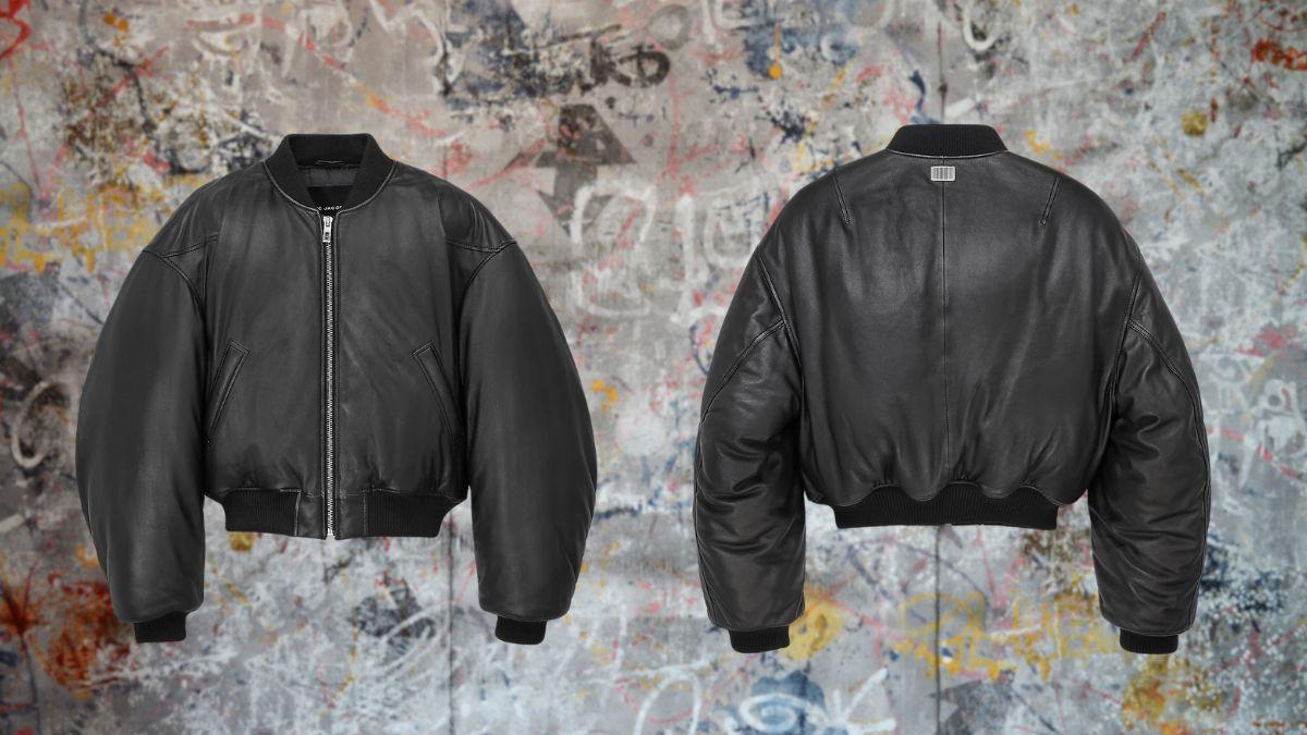 A black puffy leather bomber jacket with a zip-up front, ribbed cuffs, and an oversized design, shown from the front and back against a graffiti-style background.