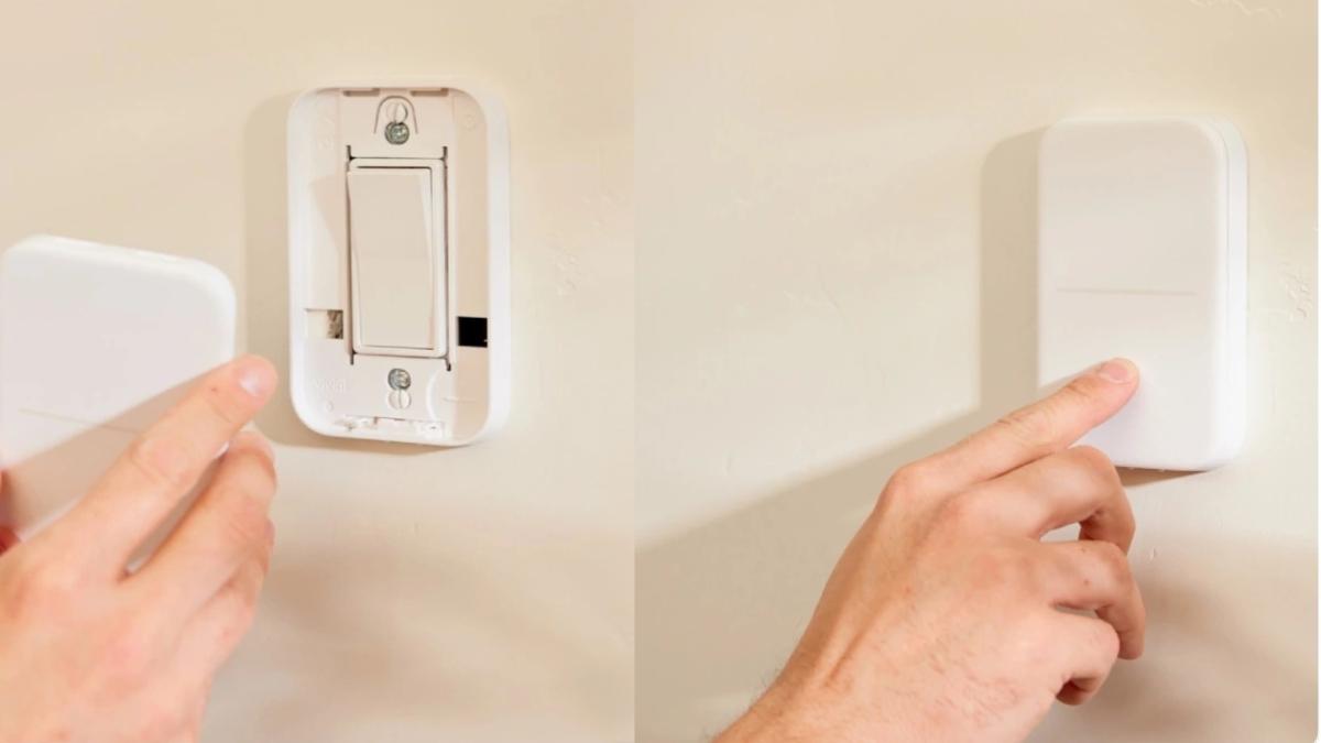A person installs or adjusts a smart light switch cover on a wall, demonstrating home automation setup.