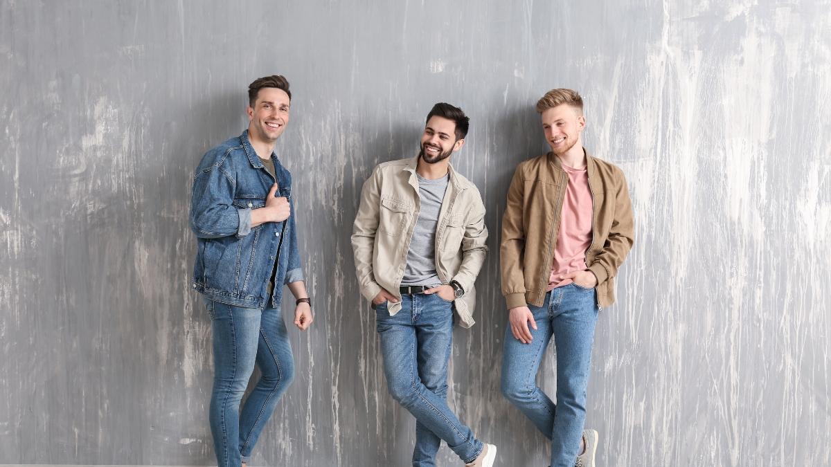 Three stylish men wearing casual denim and neutral jackets, posing against a gray textured wall — showcasing modern men’s fashion from the COOFANDY Holiday Season Collection.
