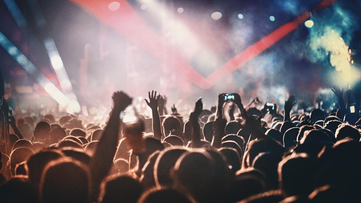 Excited crowd raising hands at a live concert with colorful stage lights and smoke in the background – perfect visual for StubHub Gift Cards and live event experiences.