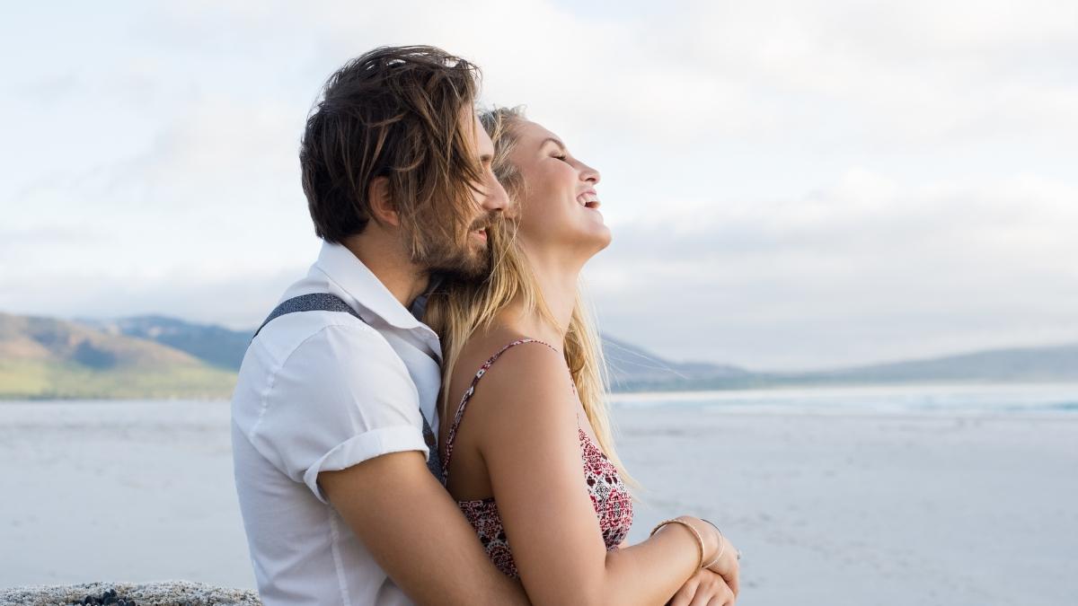 Happy couple embracing by the beach, smiling and enjoying a peaceful moment together, symbolizing intimacy, connection, and confidence