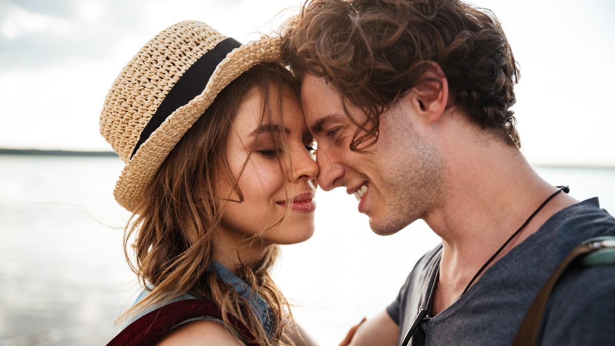 Close-up of a smiling couple touching foreheads by the beach, expressing love, intimacy, and emotional connection