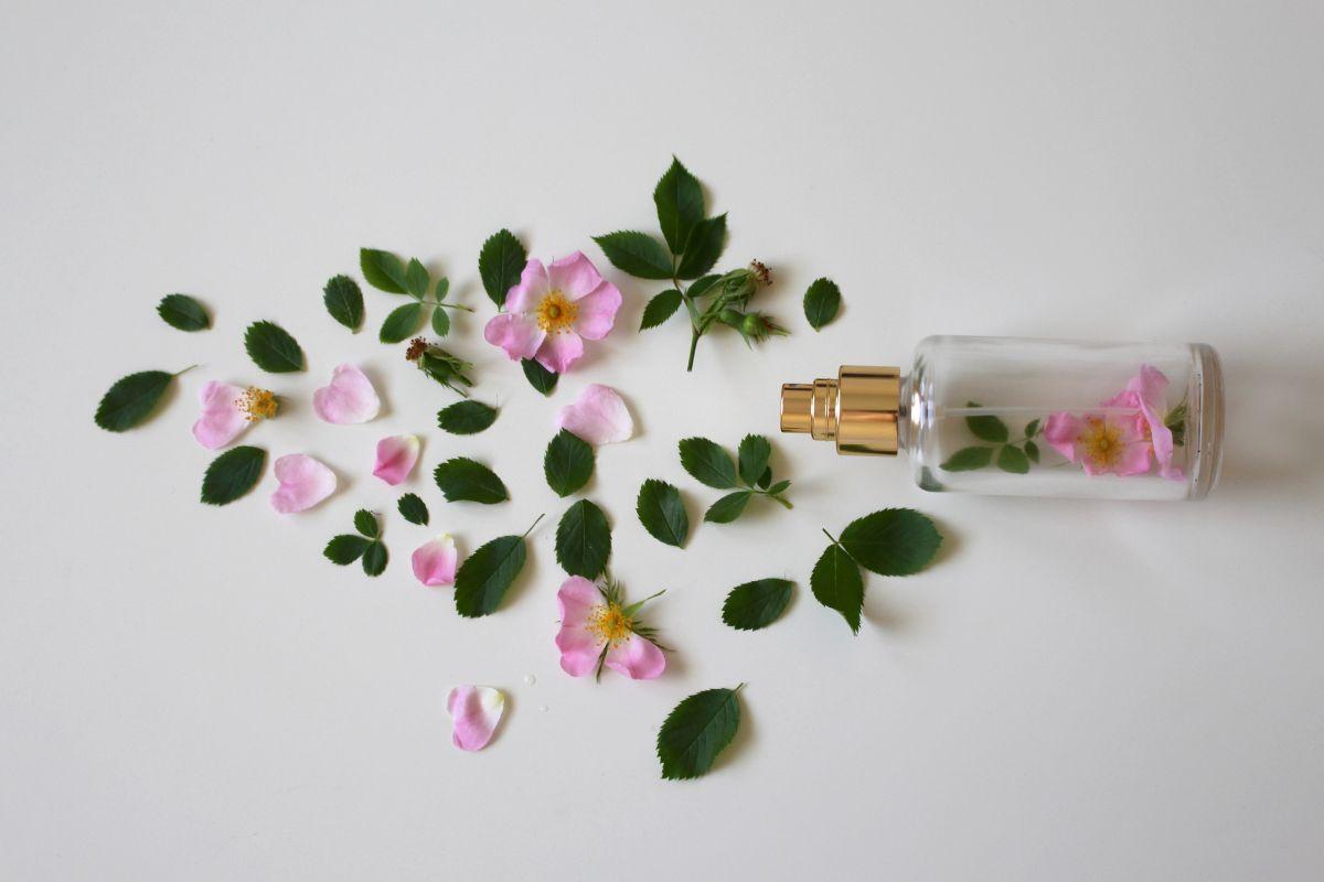 Perfume bottle with scattered pink flower petals and green leaves arranged on a white background.