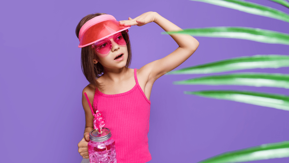 A young girl wearing a pink visor, matching sunglasses, and a pink tank top, holding a jar with a curly straw, set against a vibrant purple background with green palm leaves.