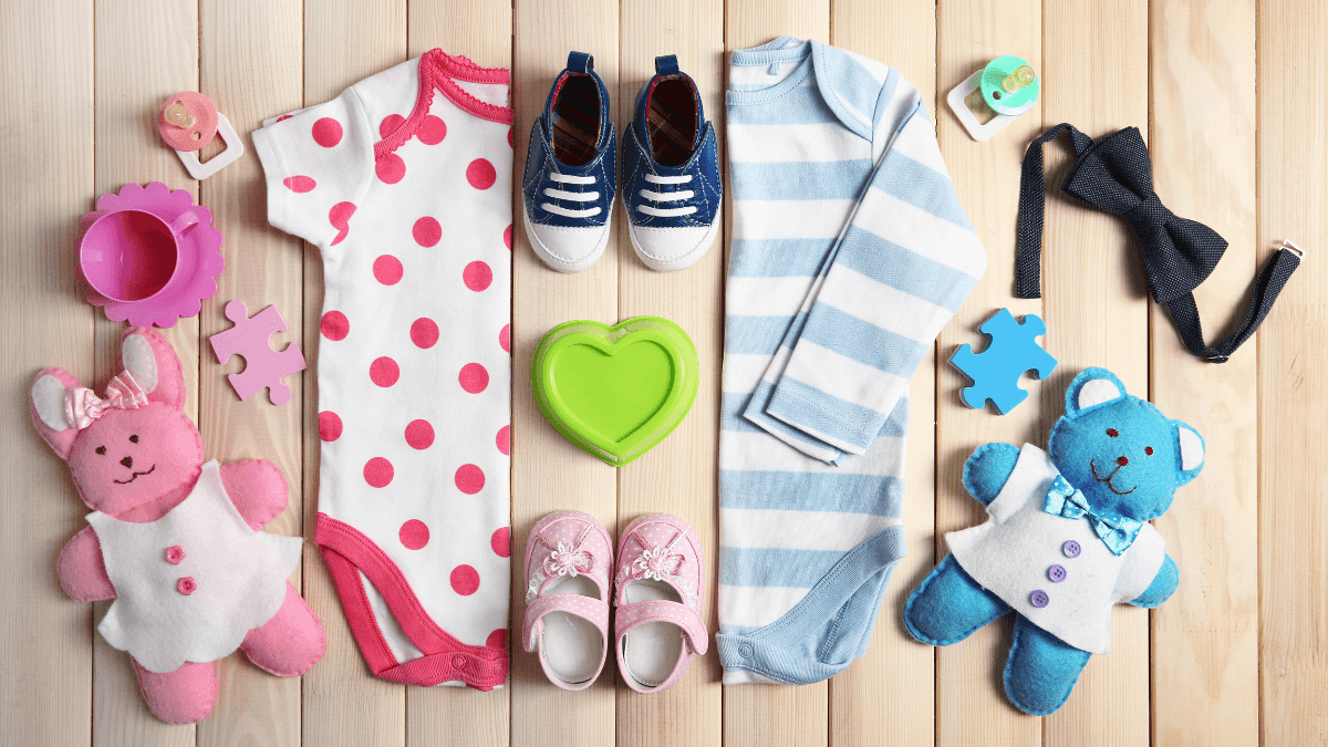 A flat lay of baby essentials, including a polka-dotted onesie, striped onesie, plush toys, baby shoes, a pacifier, and puzzle pieces, all arranged on a wooden background.