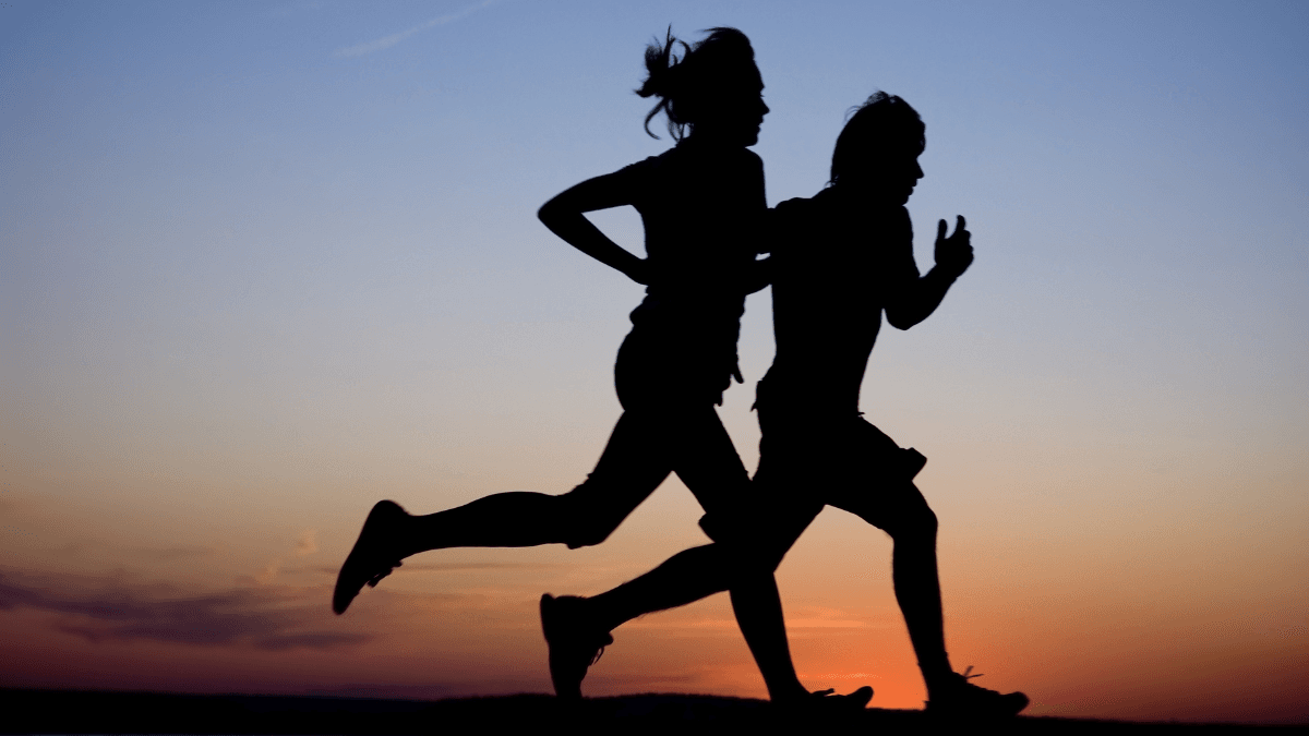 Silhouette of two people jogging against a vibrant sunset sky, capturing movement and energy.