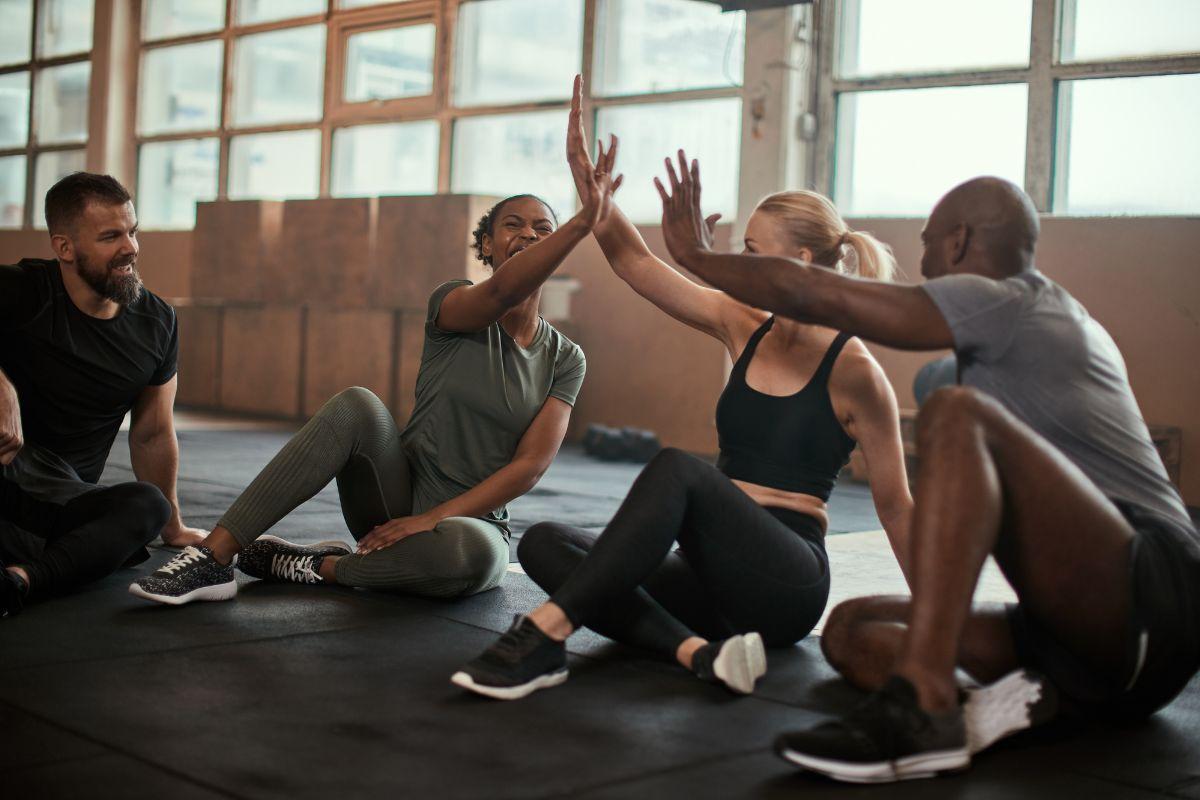 Group of people sitting on the gym floor, smiling and giving high-fives after a workout.