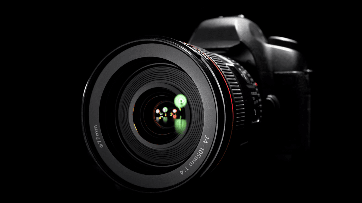 Close-up of a professional camera lens with reflections, showcasing precision optics against a dramatic black background.