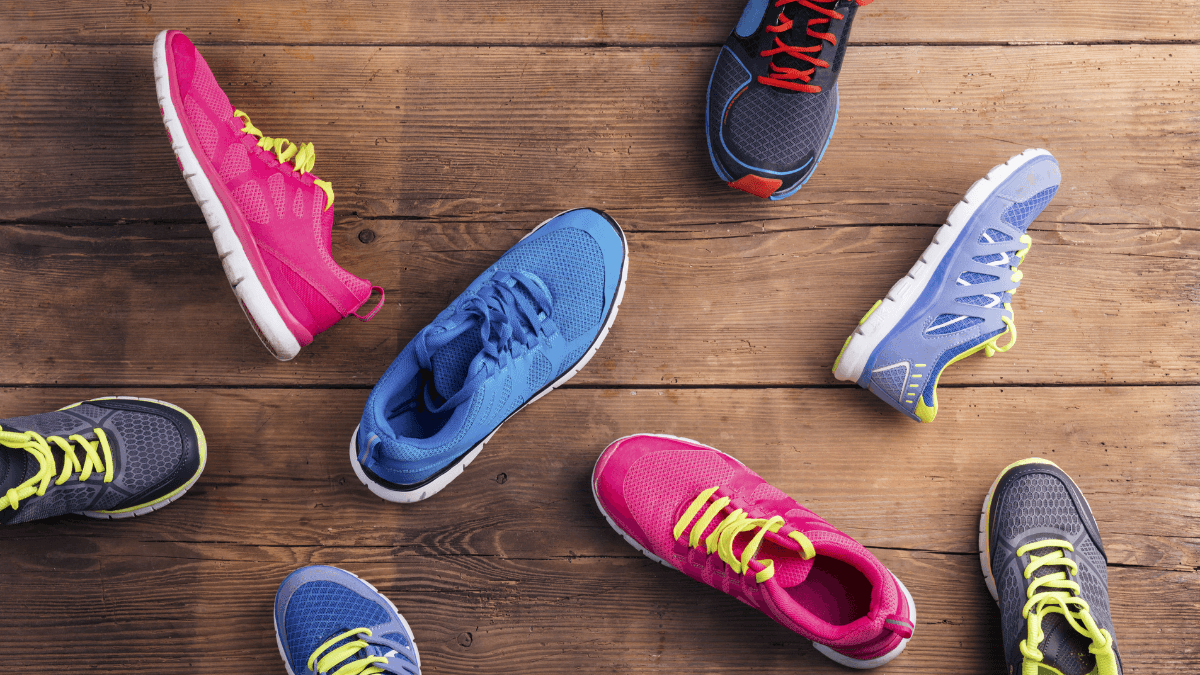 A variety of colorful athletic running shoes, including shades of pink, blue, and gray, scattered on a wooden floor in an arrangement suggesting a playful or casual display.
