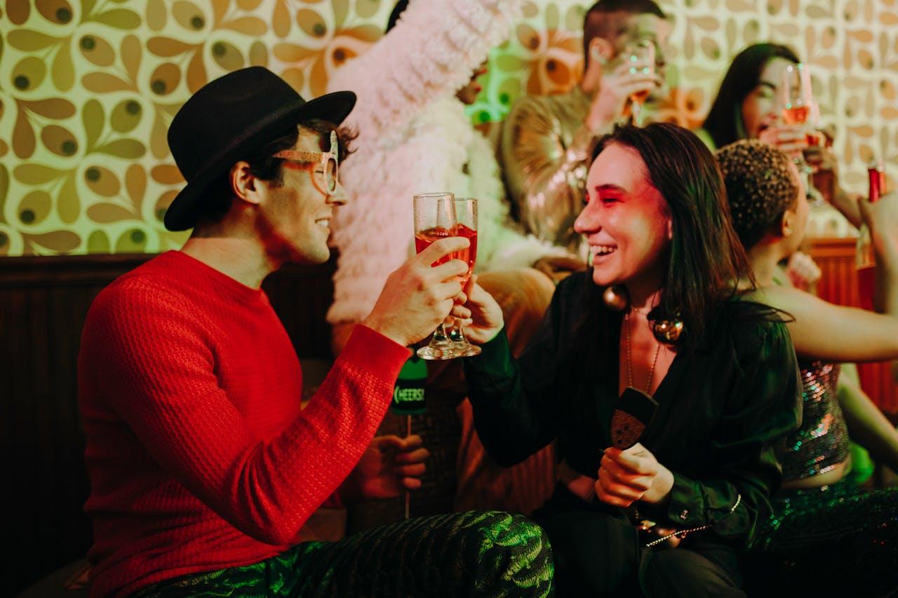Friends in colorful outfits clinking glasses and laughing at a festive party, sharing a fun moment with drinks and celebration.
