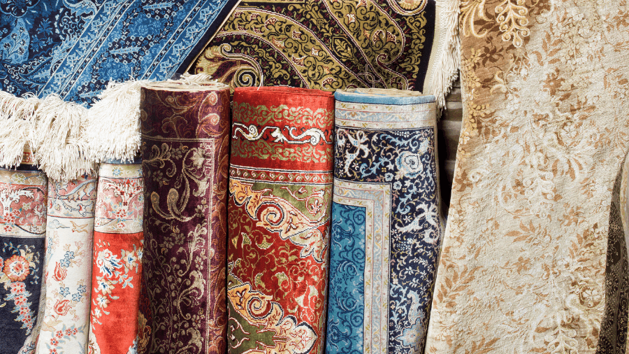 Colorful assortment of rolled-up Persian and oriental rugs with intricate patterns and rich textures, showcasing traditional craftsmanship and elegance.