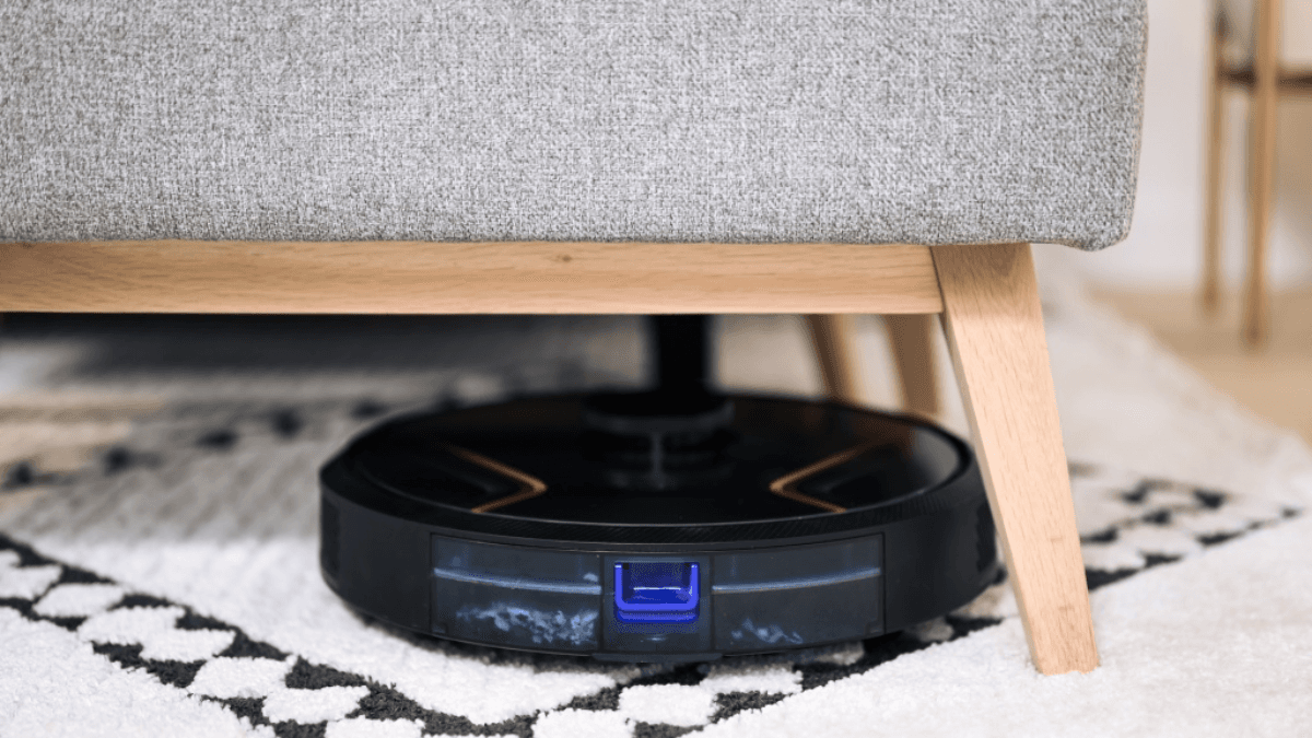 A sleek robot vacuum cleaner maneuvering under a couch, showcasing its ability to clean hard-to-reach areas effortlessly for a tidy and dust-free living space.