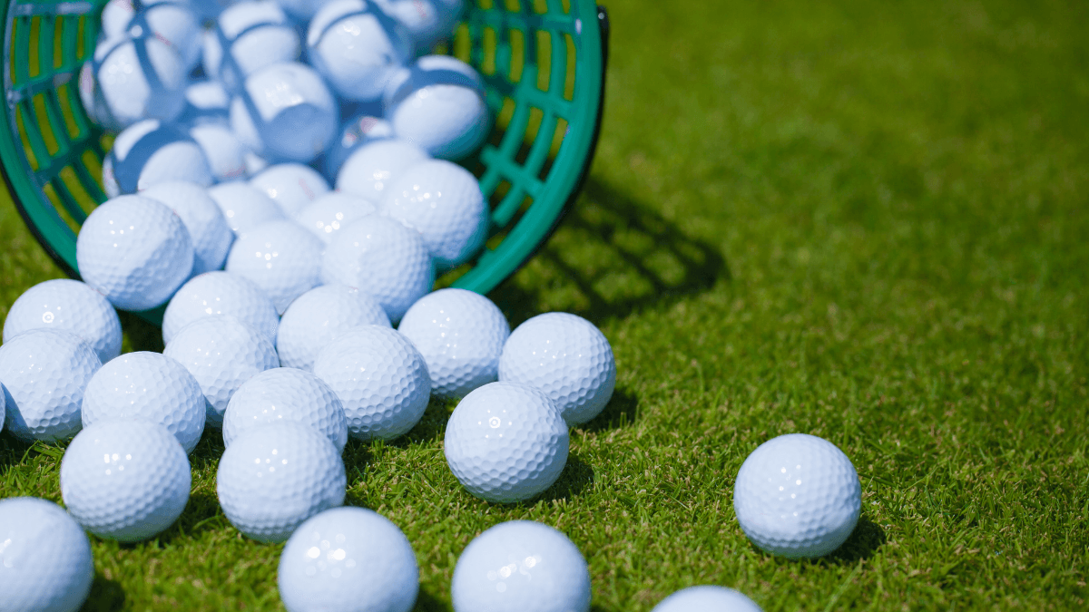 A basket of white golf balls tipped over on a lush green field, showcasing a perfect practice setup under bright daylight.
