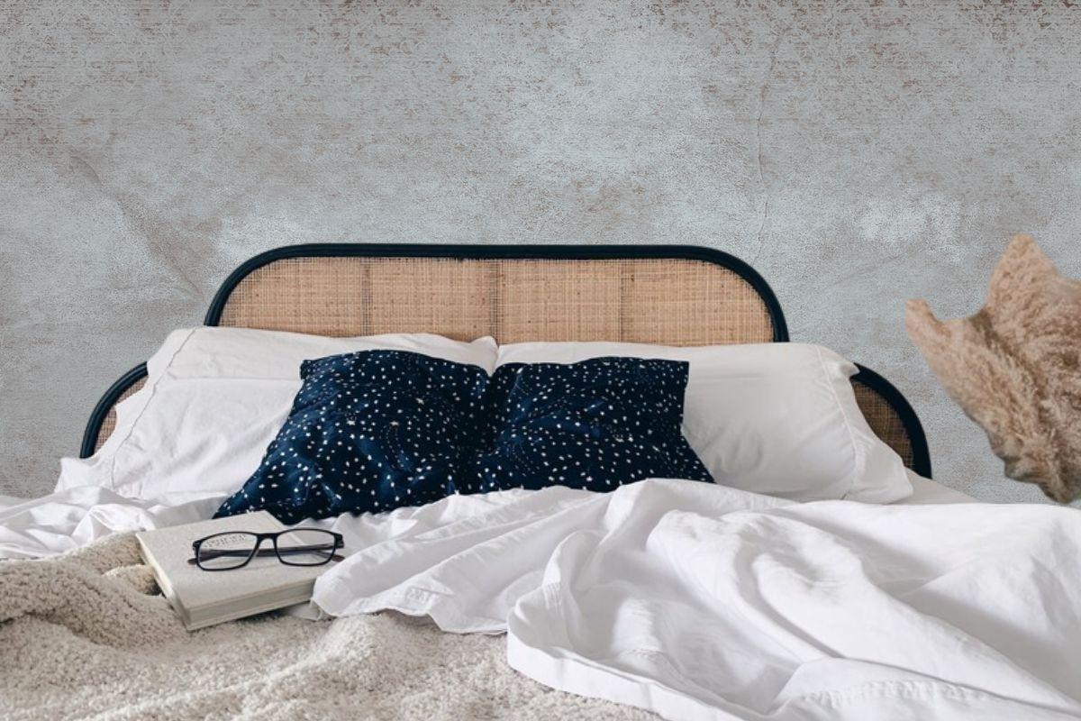Cozy bed with a woven rattan headboard, white bedding, navy blue star-patterned pillows, and a book with glasses resting on the blanket.