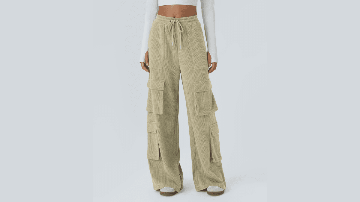 A model wearing beige corduroy cargo pants with multiple pockets, a drawstring waist, and wide legs, paired with a long-sleeve white crop top, standing against a light gray background.