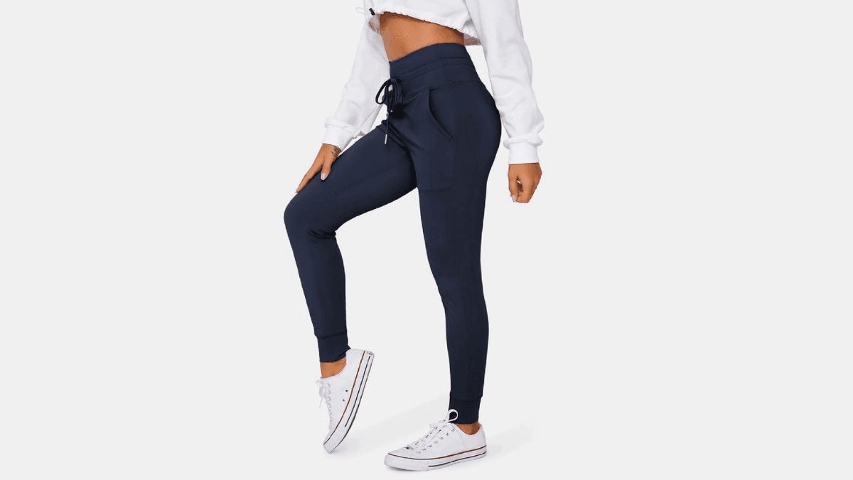 A model wearing navy joggers with a drawstring waist, paired with white sneakers and a white cropped sweatshirt against a light gray background.