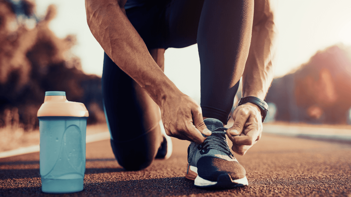 Close-up of a runner tying shoelaces on athletic shoes, with a blue water bottle on a running track during sunrise.