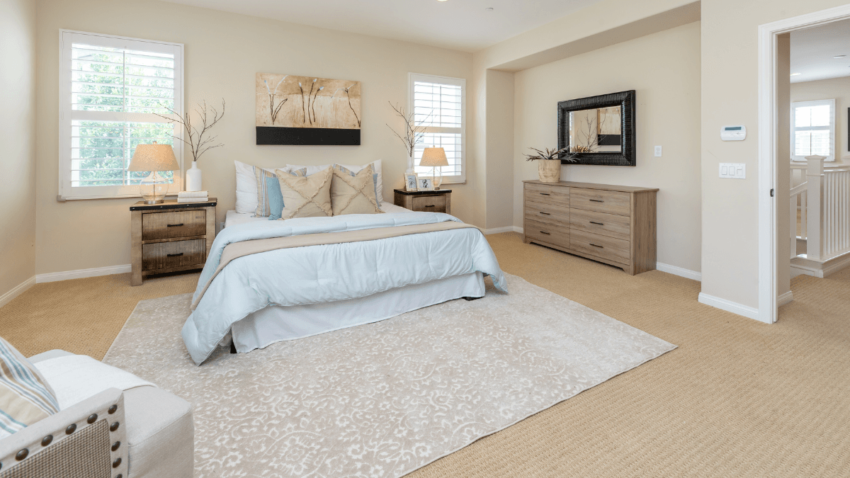 Spacious bedroom with a light blue and beige color palette, featuring cozy bedding and elegant wooden furniture.