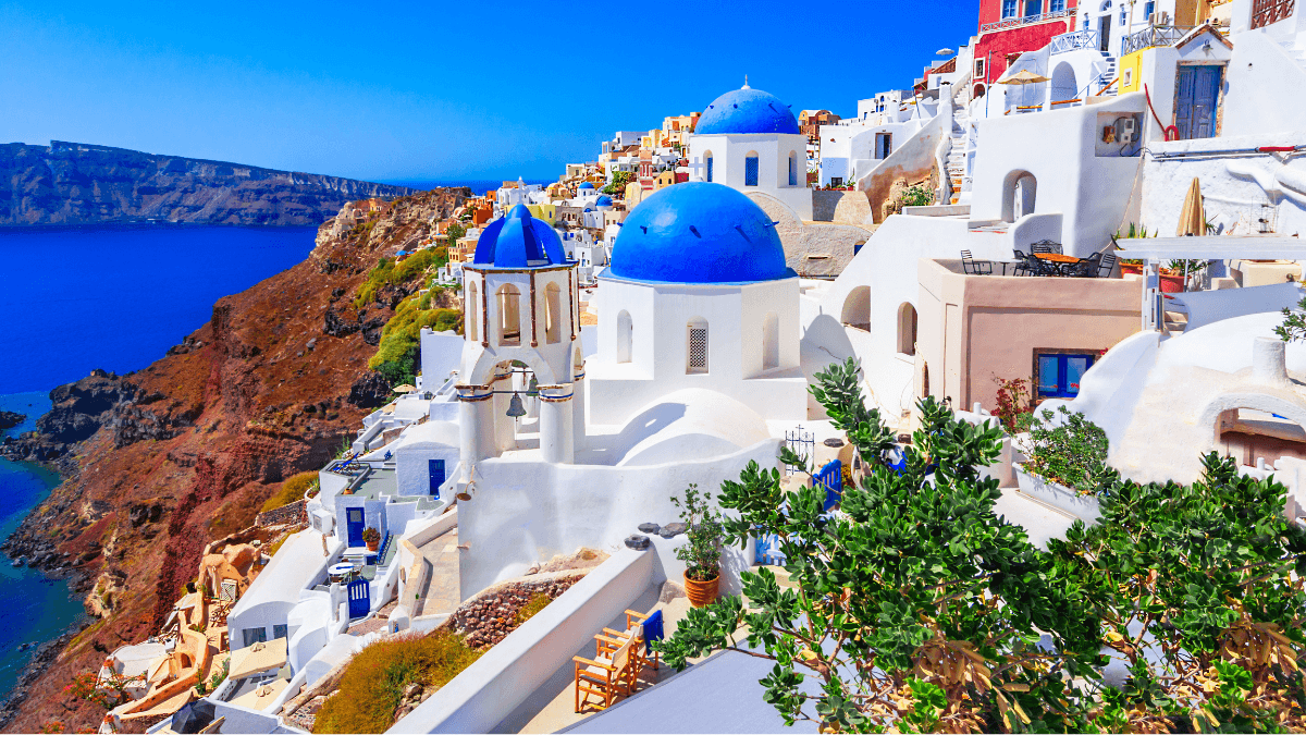 Iconic view of Santorini, Greece, showcasing whitewashed buildings with blue domes perched on cliffs overlooking the Aegean Sea.