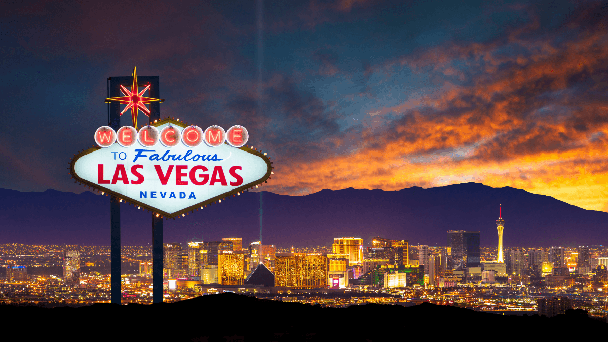 Illuminated Las Vegas sign with the vibrant city skyline in the background, set against a dramatic sunset.
