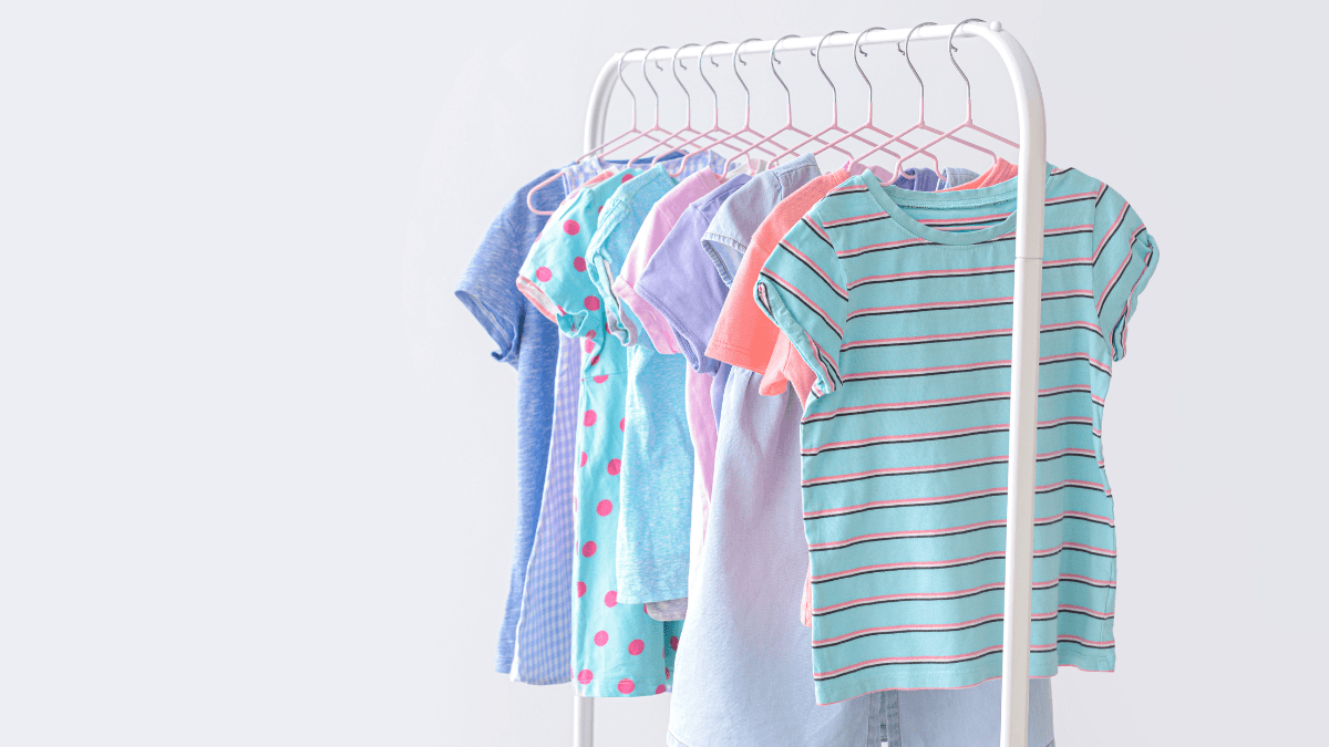 A clothing rack displaying colorful children's shirts, featuring stripes, polka dots, and solid patterns in pastel and bright tones.