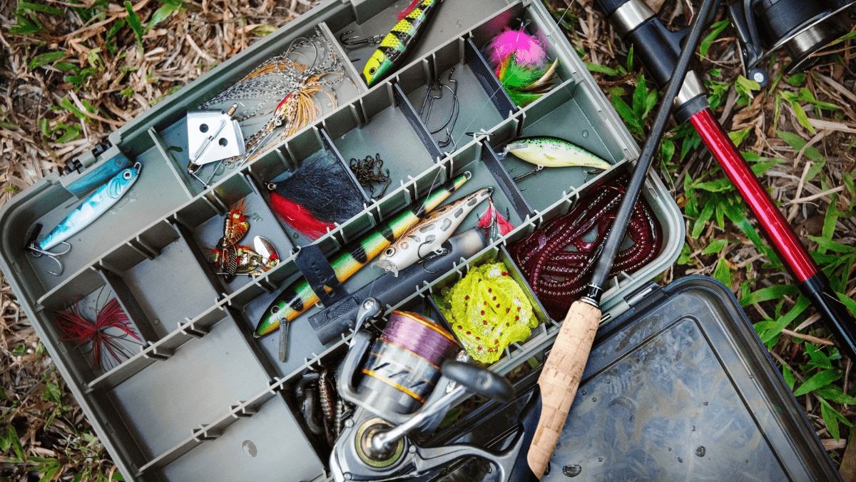A fishing tackle box filled with lures, hooks, and bait, alongside a spinning reel and fishing rod. Ideal for anglers preparing for a fishing trip.