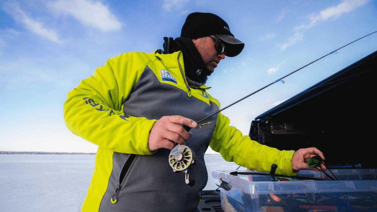 An ice fisherman dressed in cold-weather gear, preparing his fishing rod near a frozen lake.