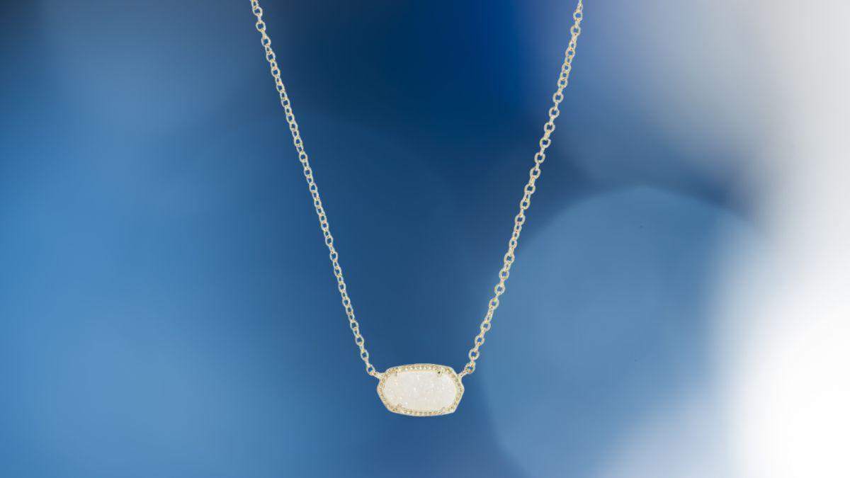 A silver chain necklace with an oval-shaped white stone pendant against a blue background.