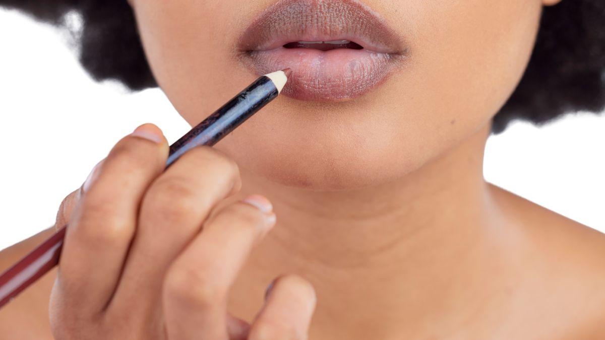 A close-up of a woman applying brown lip liner to her lips, creating a well-defined and polished look.