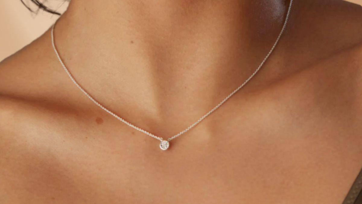 A close-up of a woman's neck wearing a delicate silver necklace with a small round diamond pendant.