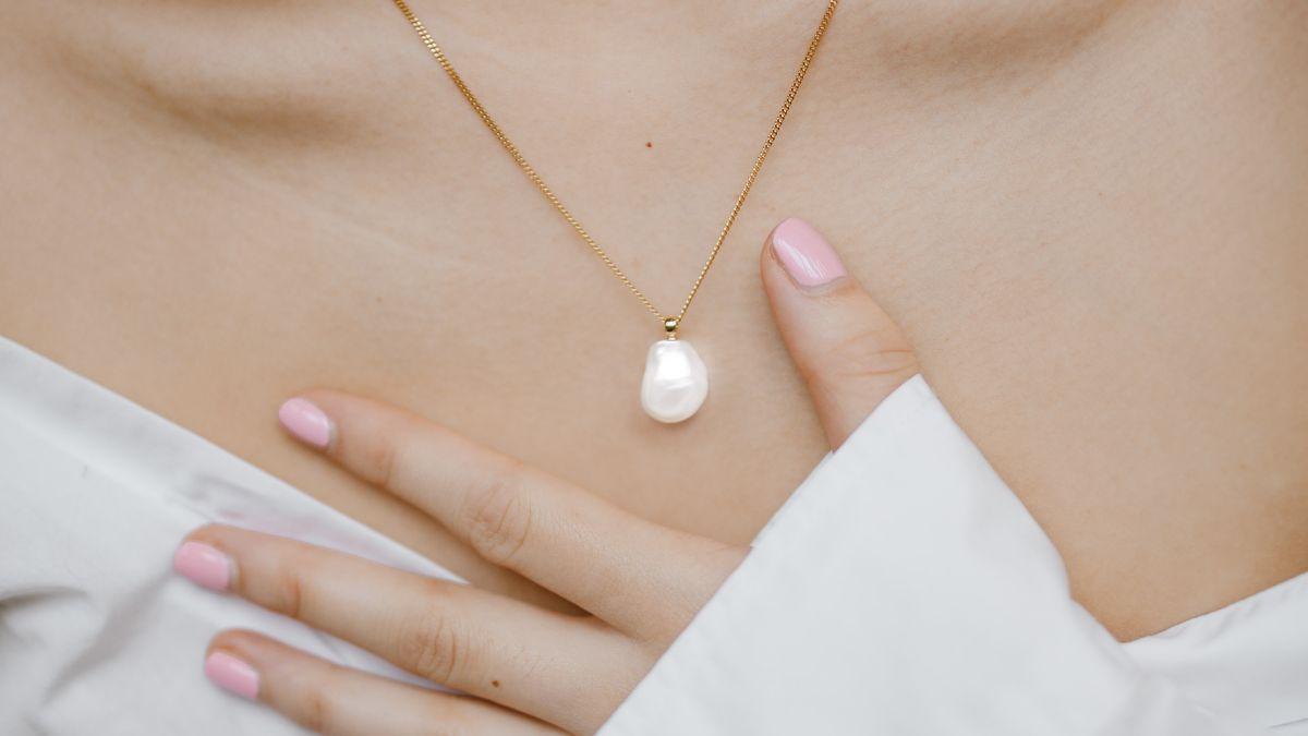 A woman wears a gold necklace with a single white pearl pendant.