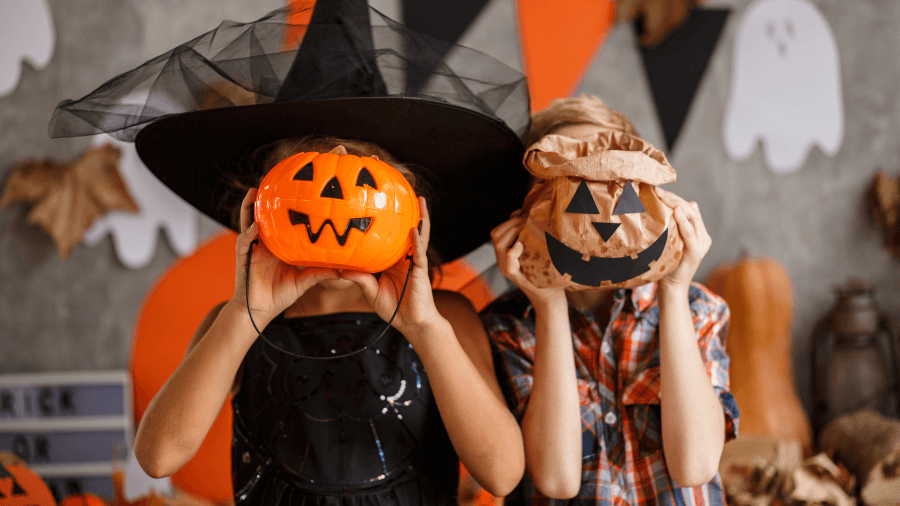 Two children in Halloween costumes holding pumpkin-themed decorations in front of their faces.